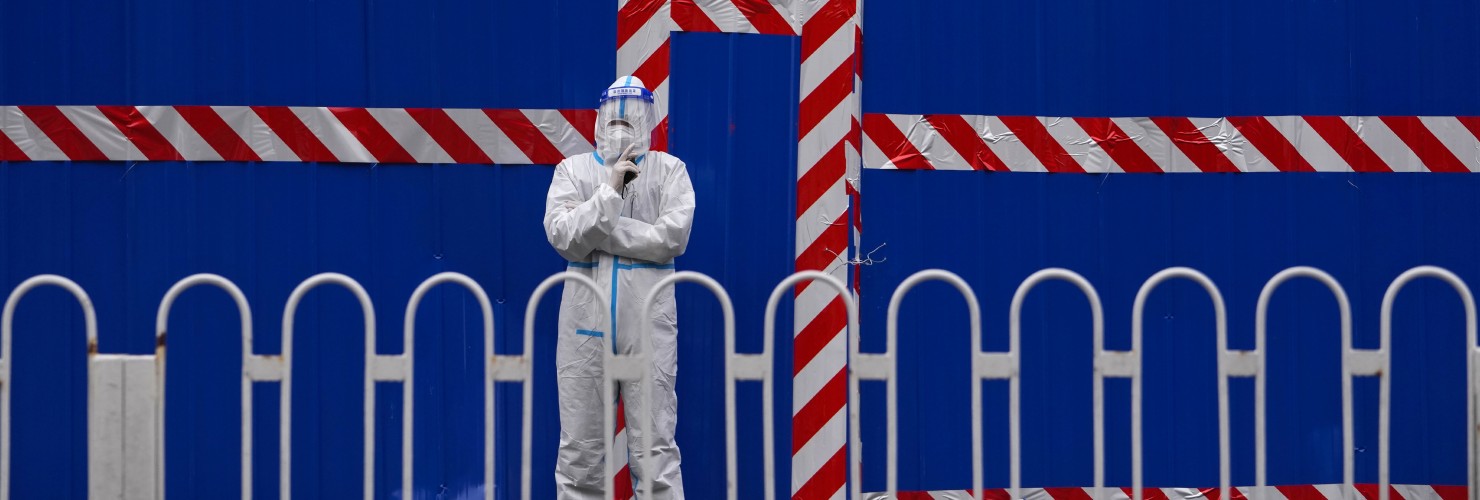 A security guard wearing a protective suit stand watch over a barricaded community that was locked down for health monitoring following the COVID-19 case detected in the area, Tuesday, March 22, 2021, in Beijing