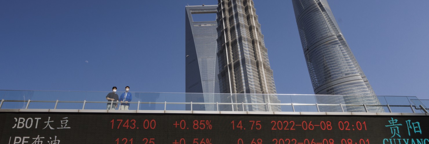 People stand on pedestrian bridge showing stock exchange data in Lujiazui