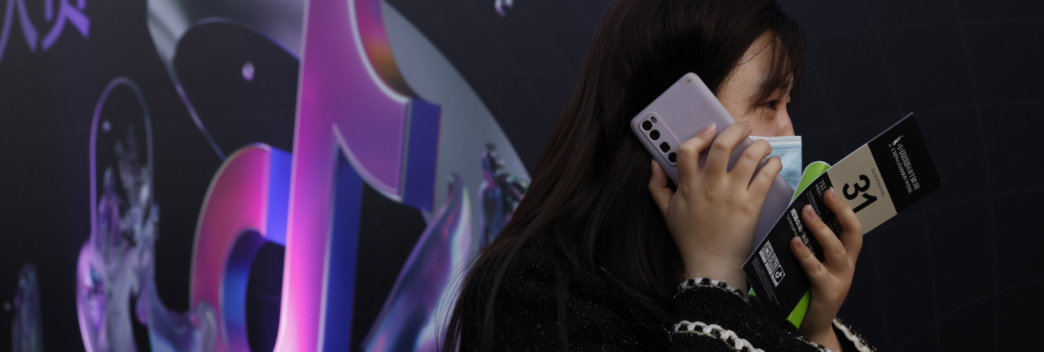 A woman speaks on her phone near the logo for Douyin in Beijing 