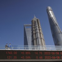 People stand on pedestrian bridge showing stock exchange data in Lujiazui