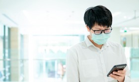 A man wearing a facemask looks at his smartphone