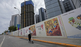 A girl wearing a face mask to help protect from the coronavirus rides a scooter past Chinese government's propaganda "China Dream" billboard on display along a commercial office buildings under construction in Tongzhou, outskirts of Beijing.