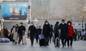 Passengers wearing face masks walk with their luggage in front of the Beijing Railway Station in Beijing, China, 10 January 2023.