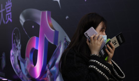 A woman speaks on her phone near the logo for Douyin in Beijing 